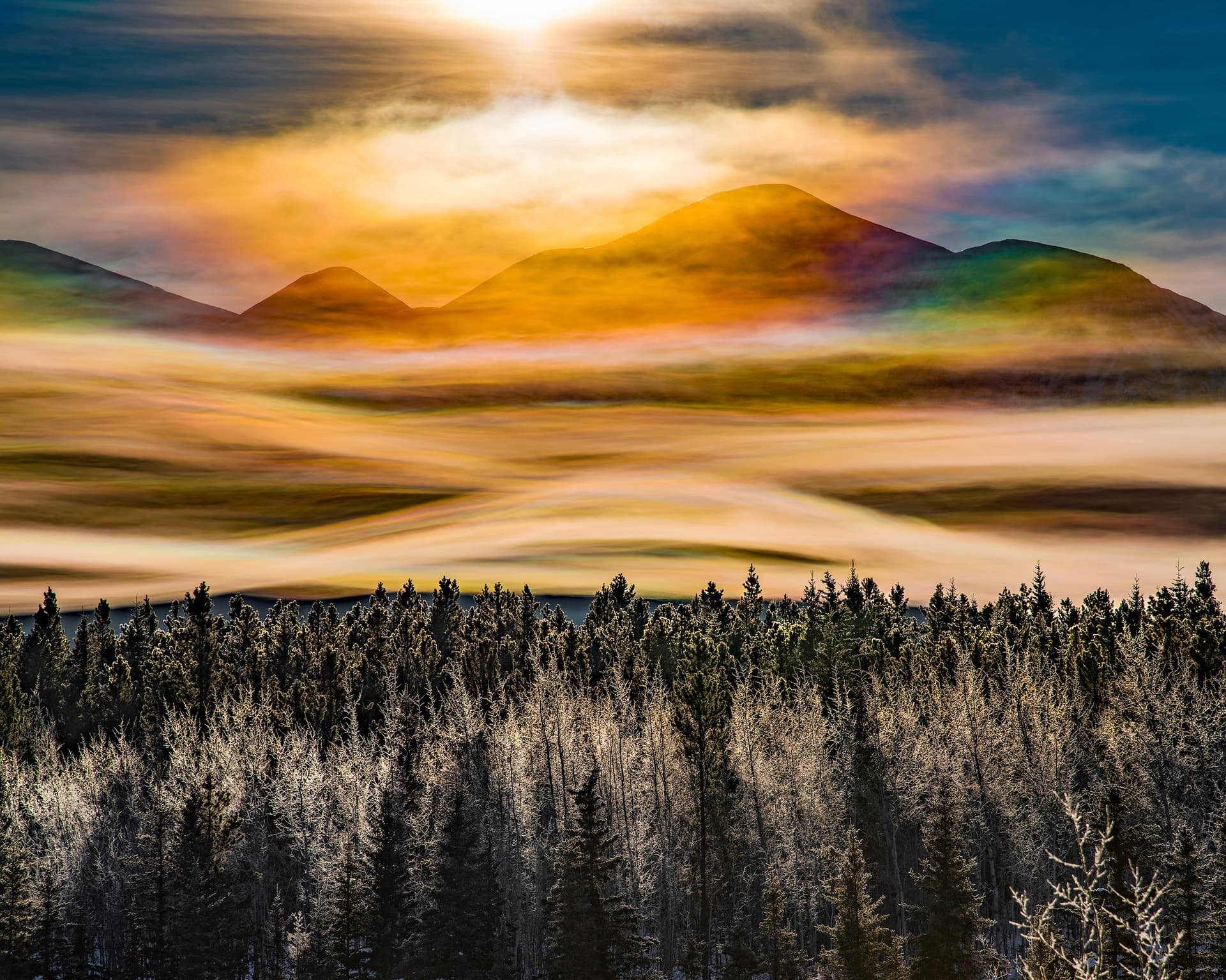 Yukon mountains at dawn with iridescent clouds above forested slopes and a mist-filled valley